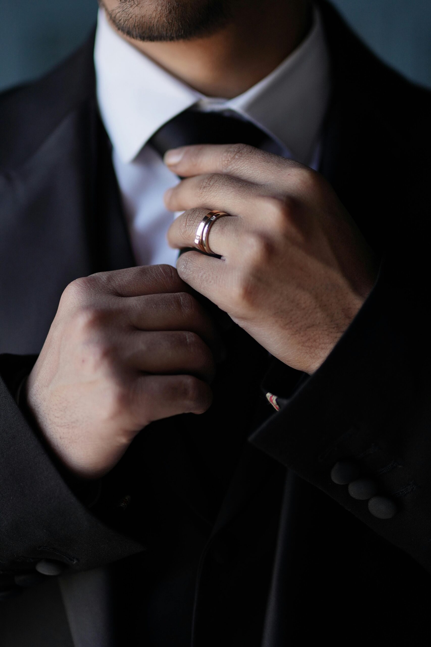 Sophisticated man adjusts necktie with ring, showcasing elegance and fashion.