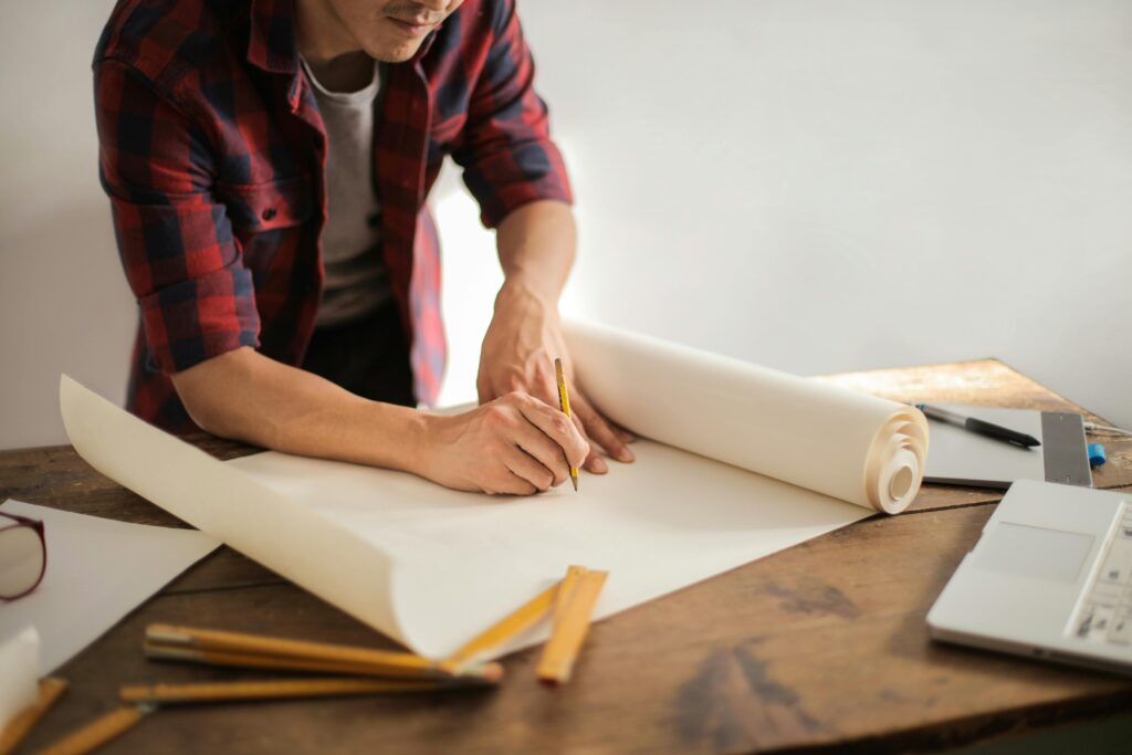 pexels-photo-3760529-3760529 A focused architectural designer drafting blueprints at a desk indoors.